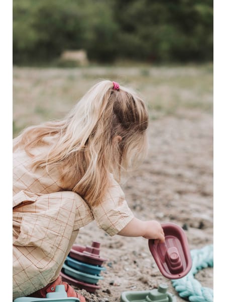 En samling af små legebåde arrangeret i en halvcirkel i farverne turkis, rød, blå og grå.
